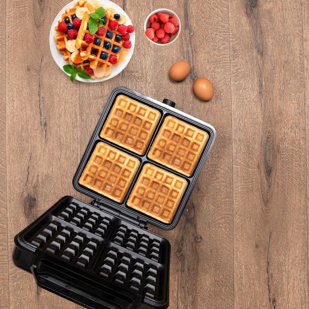 Otwarta gofrownica Alpinastojąc na blacie . W środku smażą się 4 gofry. Zdjęcie od góry, obok stoją gofry z owocami.